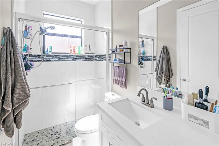 Full bathroom featuring a walk-in shower with mosaic tile accents, a floating vanity with an integrated sink, and a framed mirror