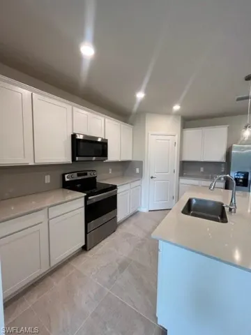 Kitchen with light countertops, stove, tasteful backsplash, a sink, and white cabinets