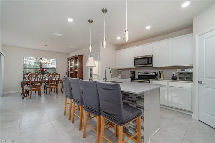 Kitchen featuring white cabinets, stainless steel appliances, hanging light fixtures, and an island with sink