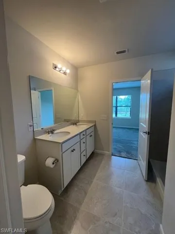 Full bathroom with double vanity, visible vents, toilet, and a sink