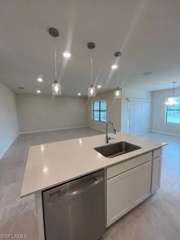 Kitchen featuring a kitchen island with sink, a sink, dishwashing machine, decorative light fixtures, and open floor plan