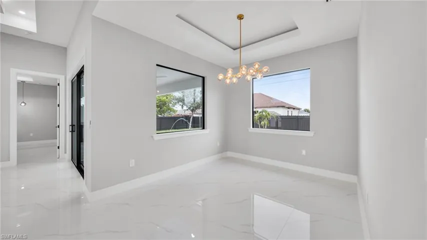 Unfurnished dining area featuring light marble finish floors, healthy amount of natural light, a tray ceiling, and a chandelier