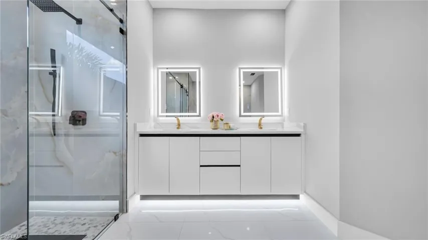 Full bath featuring a marble finish shower, double vanity, and light marble finish flooring
