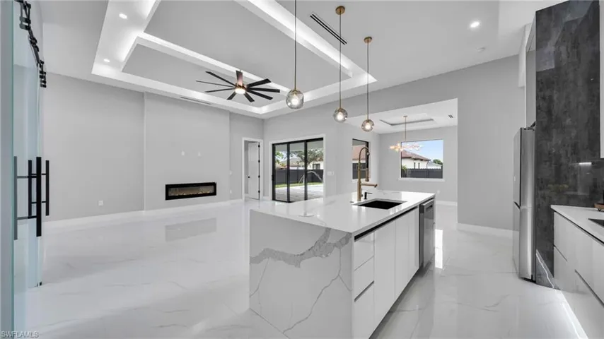 Kitchen with a tray ceiling, modern cabinets, white cabinets, a glass covered fireplace, and a ceiling fan