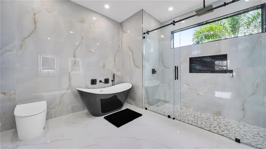 Bathroom with tile walls, a marble finish shower, marble tiled flooring, a freestanding tub, and recessed lighting