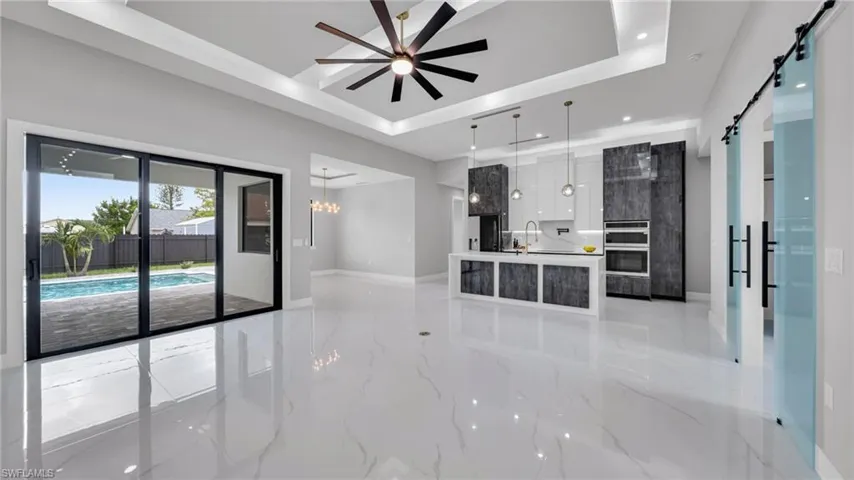 Unfurnished living room with a raised ceiling, a barn door, light marble finish flooring, a ceiling fan, and recessed lighting