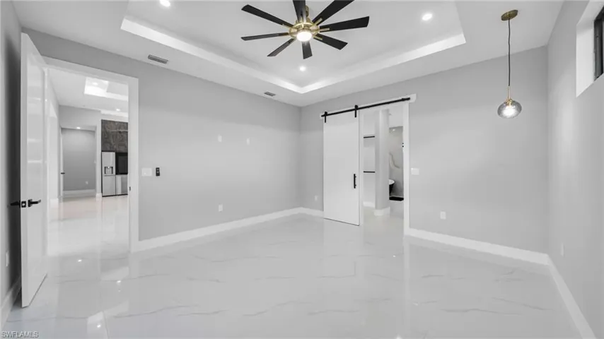 Unfurnished bedroom featuring a barn door, light marble finish flooring, recessed lighting, and a raised ceiling