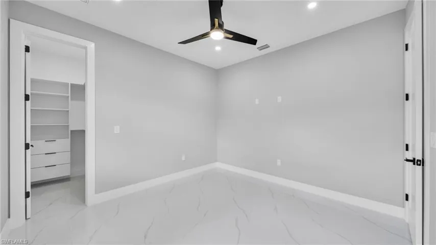 Unfurnished bedroom with light marble finish floors, a walk in closet, a ceiling fan, and recessed lighting