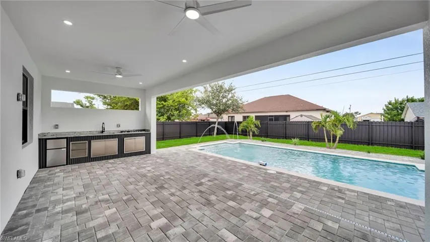 View of swimming pool featuring an outdoor kitchen, a fenced backyard, a patio area, and a ceiling fan