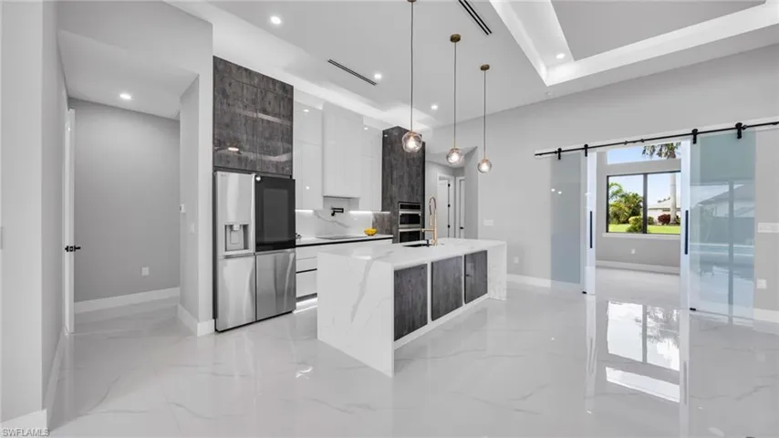 Kitchen featuring modern cabinets, white cabinets, stainless steel fridge, light marble finish flooring, and recessed lighting