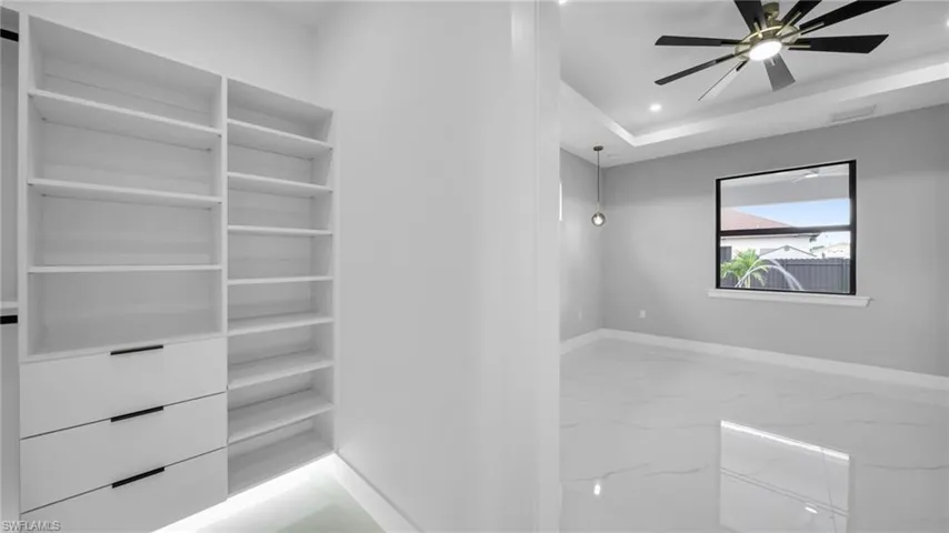 Walk in closet featuring light marble finish flooring, ceiling fan, and a tray ceiling