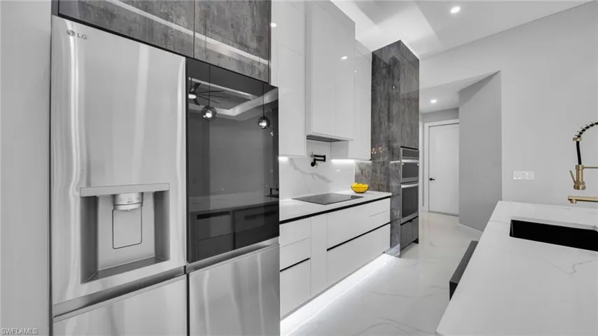 Kitchen with modern cabinets, white cabinets, stainless steel appliances, light stone countertops, and light marble finish floors