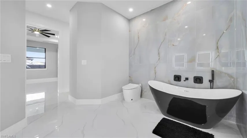 Full bathroom with marble tiled flooring, a freestanding tub, tile walls, recessed lighting, and ceiling fan