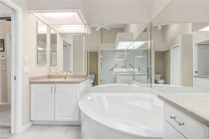 Primary bathroom featuring toilet, tile patterned flooring, vanity, independent shower and bath, and ceiling fan
