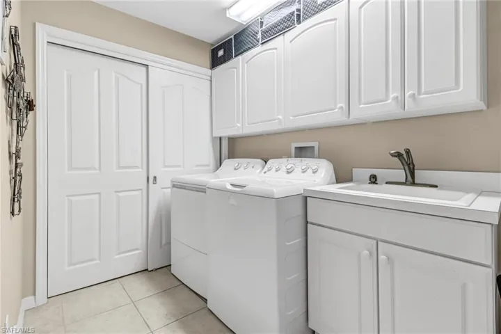 Laundry room with cabinets, sink, light tile patterned floors, and washing machine and dryer