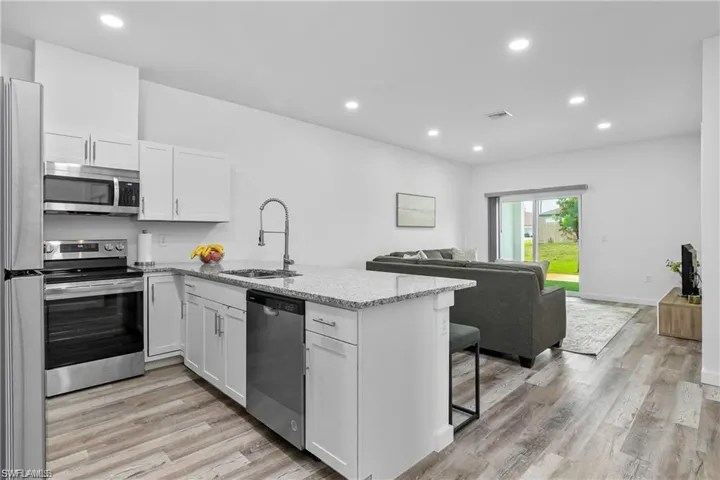 Kitchen featuring stainless steel appliances, recessed lighting, light stone countertops, open floor plan, and light wood-style floors