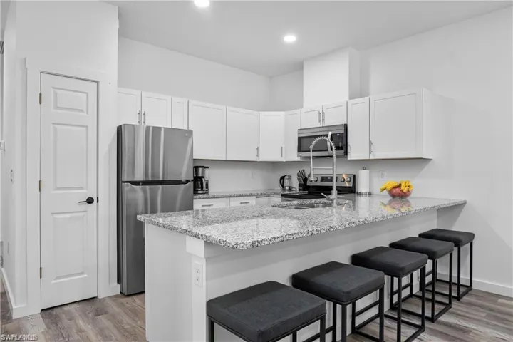 Kitchen with stainless steel appliances, light stone counters, light wood-style floors, white cabinets, and recessed lighting