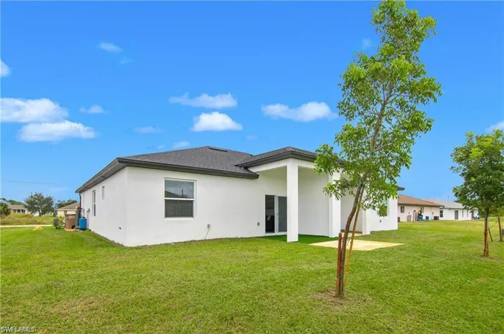 Rear view of property with a lawn, stucco siding, and a patio