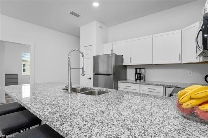 Kitchen with light stone counters, stainless steel appliances, a breakfast bar, white cabinets, and a peninsula