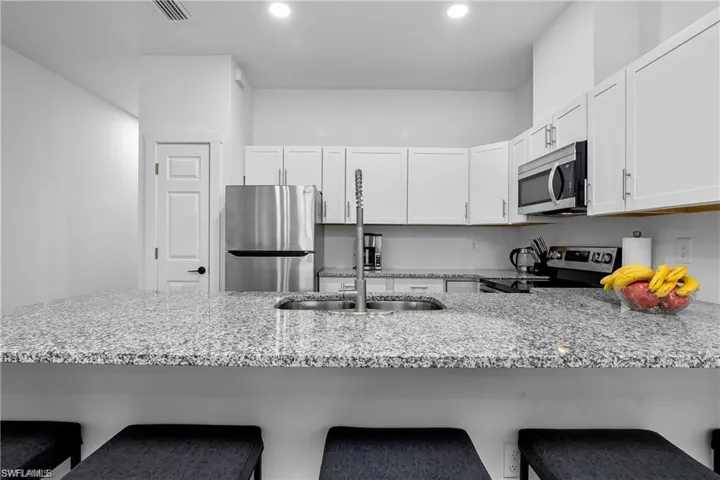 Kitchen featuring a kitchen bar, light stone countertops, appliances with stainless steel finishes, a peninsula, and white cabinetry