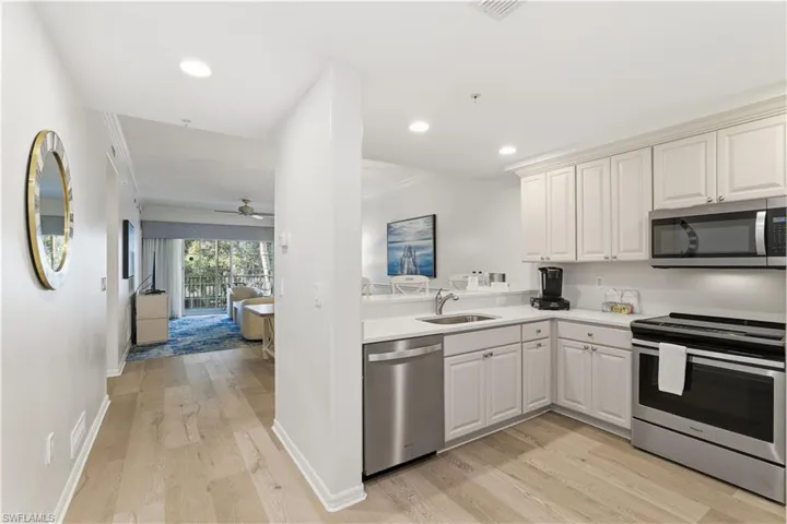 Kitchen featuring appliances with stainless steel finishes, light wood-type flooring, a ceiling fan, open floor plan, and ornamental molding