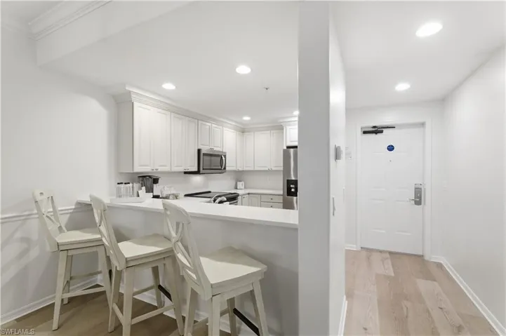 Kitchen featuring light wood-type flooring, a kitchen breakfast bar, white cabinets, recessed lighting, and stainless steel appliances