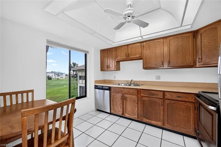 Kitchen featuring wood cabinetry, stainless steel dishwasher, tray ceiling with a center fan, and tile flooring
