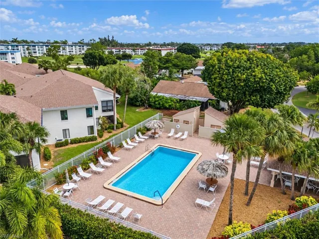 Outdoor swimming pool featuring a brick-paved deck, perimeter fencing, and mature palm trees