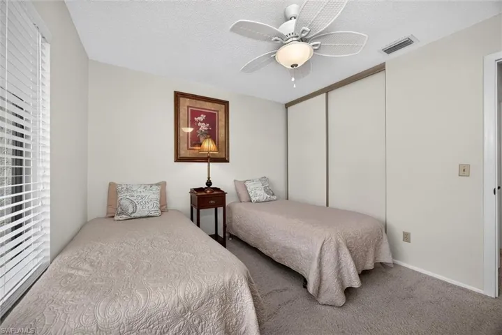 Neutral-toned bedroom featuring carpeted flooring, a white ceiling fan with integrated lighting, sliding-panel closet doors, and horizontal blinds