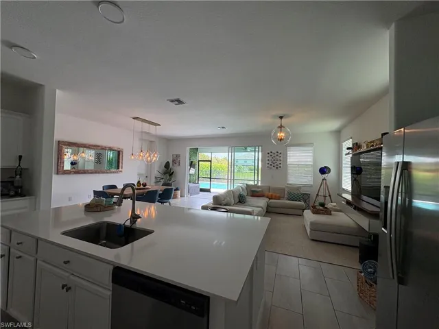 Kitchen featuring stainless steel appliances, open floor plan, white cabinets, hanging lights, and a kitchen island with sink