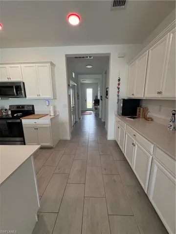 Kitchen with white cabinets, stainless steel appliances, light countertops, and wood finish floors