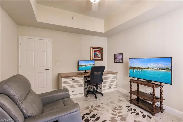 Office area with ceiling fan, light hardwood / wood-style flooring, and a raised ceiling
