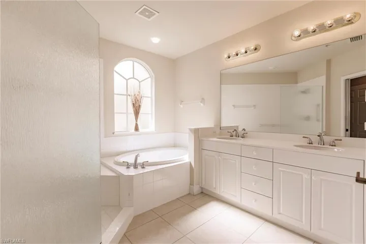 Bathroom with tile floors, vanity with extensive cabinet space, shower with separate bathtub, and double sink
