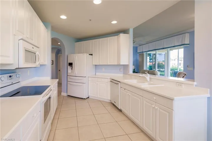 Kitchen featuring sink, white cabinets, white appliances, and light tile floors