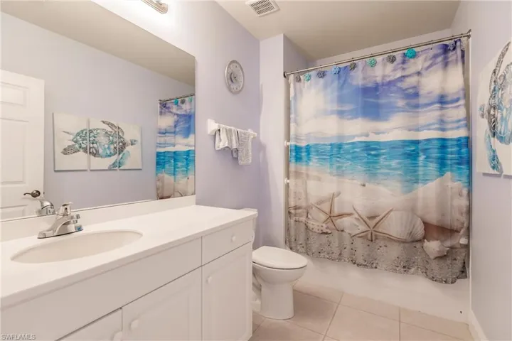Full bathroom with tile floors, shower / bath combination with curtain, large vanity, and toilet