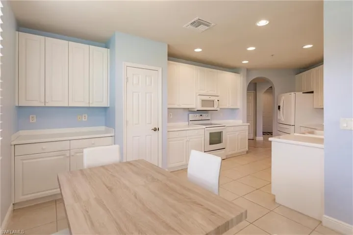 Kitchen with white cabinets, white appliances, and light tile floors