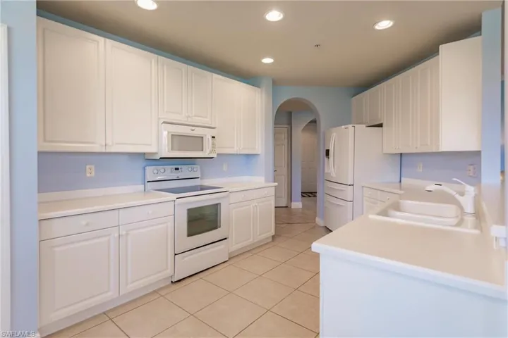 Kitchen with sink, white cabinetry, white appliances, and light tile flooring