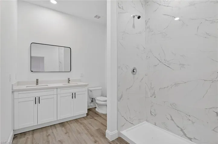 Bathroom with double vanity, light wood finished floors, and a marble finish shower
