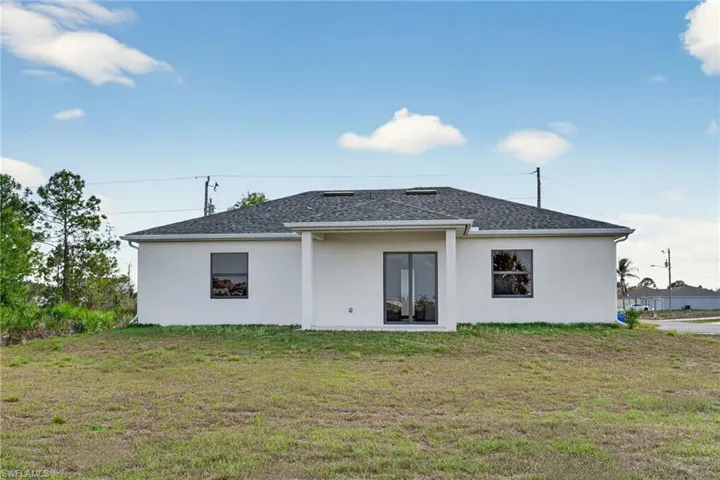 Back of property with stucco siding, a lawn, and a shingled roof