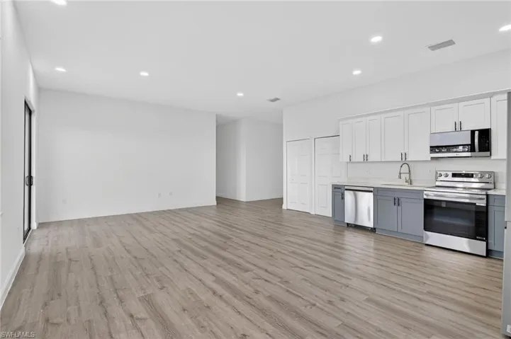 Two tone kitchen with two tone color scheme, stainless steel appliances, recessed lighting, open floor plan, and light wood-type flooring