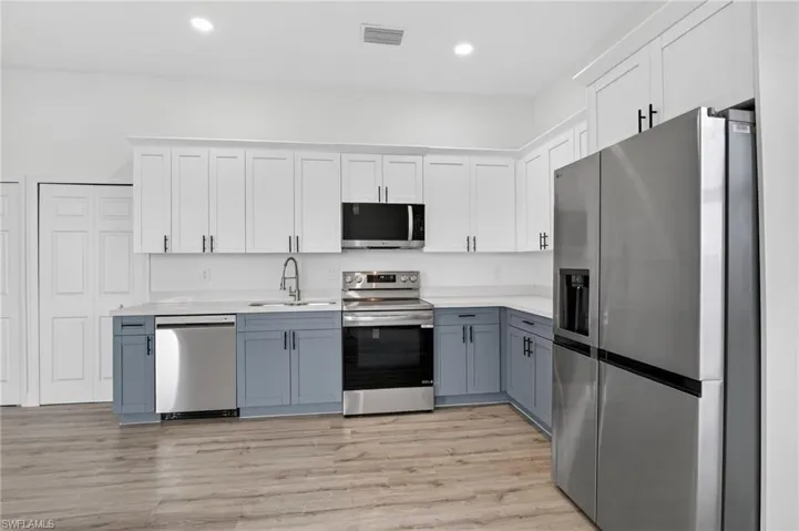 Dual tone kitchen featuring stainless steel appliances, dual tone cabinetry, light wood finished floors, light stone counters, and recessed lighting