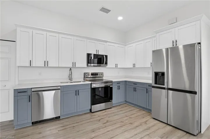 Kitchen with dual tone cabinets, stainless steel appliances, light wood finished floors, recessed lighting, and light stone counters