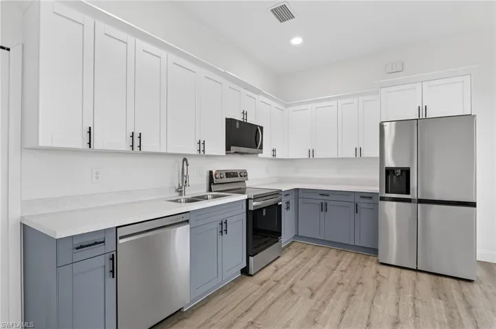 Kitchen featuring two tone cabinets, stainless steel appliances, light wood-style floors, light stone countertops, and recessed lighting