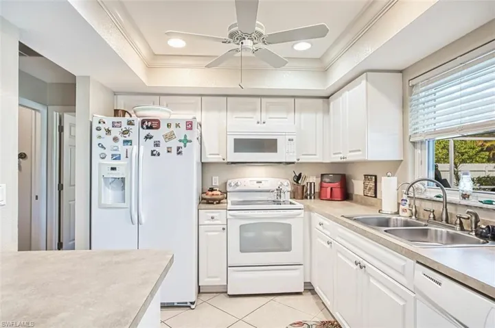 Kitchen featuring white appliances, light tile patterned floors, a raised ceiling, a sink, and white cabinets