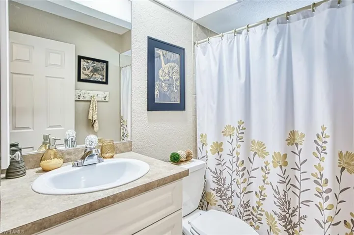 Bathroom featuring vanity, toilet, a textured wall, a skylight, and curtained shower