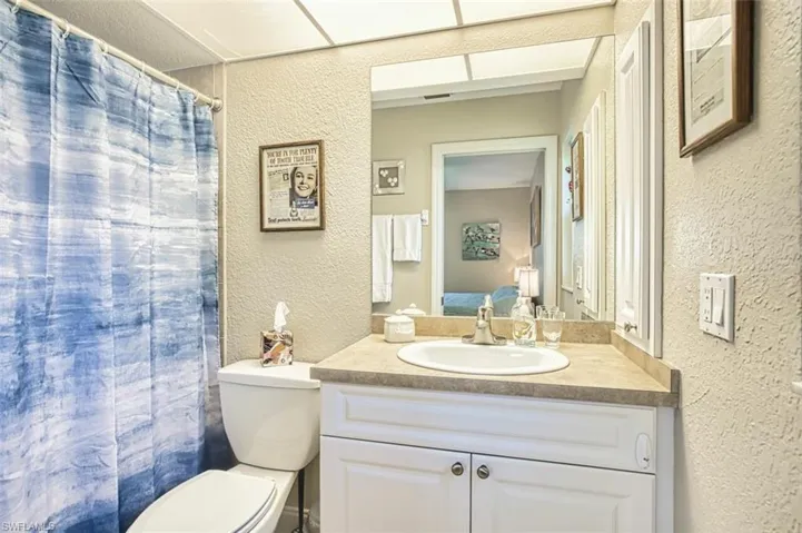 Bathroom featuring curtained shower, toilet, vanity, and a textured wall