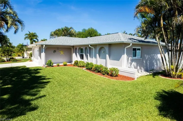 Ranch-style home with a front yard, driveway, stucco siding, and roof with shingles