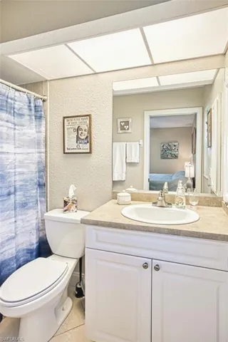 Full bath with tile patterned floors, toilet, curtained shower, vanity, and a textured wall