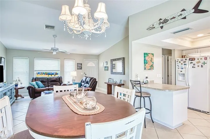 Dining room featuring light tile patterned flooring, ceiling fan with notable chandelier, lofted ceiling, and visible vents