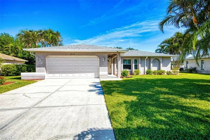 Ranch-style home with stucco siding, driveway, a garage, and a front lawn